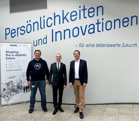 Bild von drei Männern in der Aula der THI mit einem Banner von VDE Bayern im Hintergrund