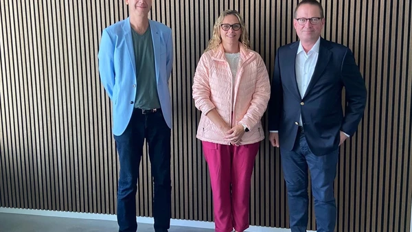 Gruppenbild bestehend aus drei Personen vor einer mit Holz verkleideten Wand