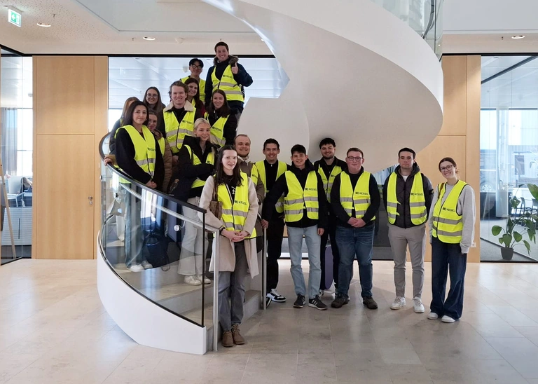 Group photo on a spiral staircase, all wearing yellow safety vests.